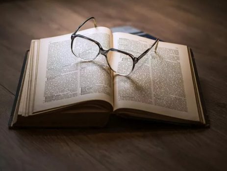 a imagem retrata um óculos de grau sobre um livro aberto