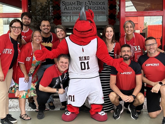 professores e o mascote Rino em frente à entrada do colégio