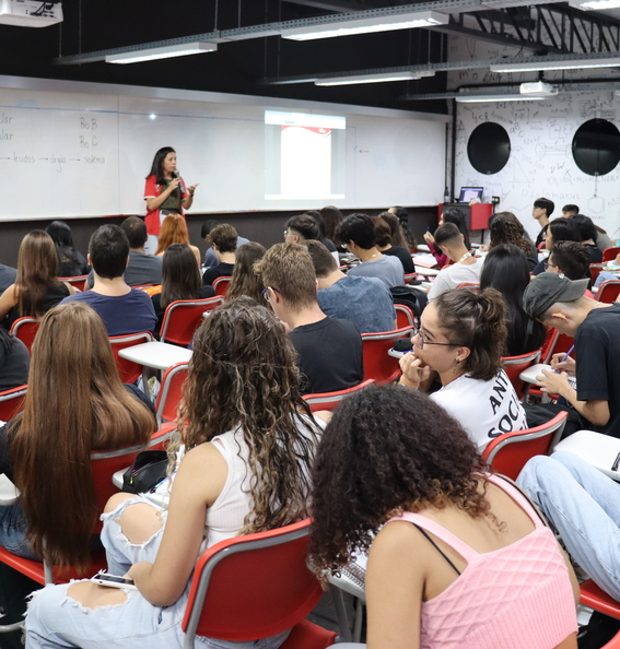 imagem da sala de aula do curso pré-vestibular da oficina do estudante repleta de alunos e uma professora de fundo