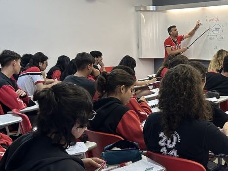 Wander Azanha durante uma aula de física. Alunos no plano principal e o professor, plano secundário