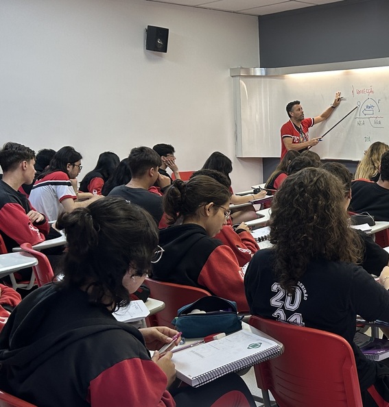 Wander Azanha durante uma aula de física. Alunos no plano principal e o professor, plano secundário